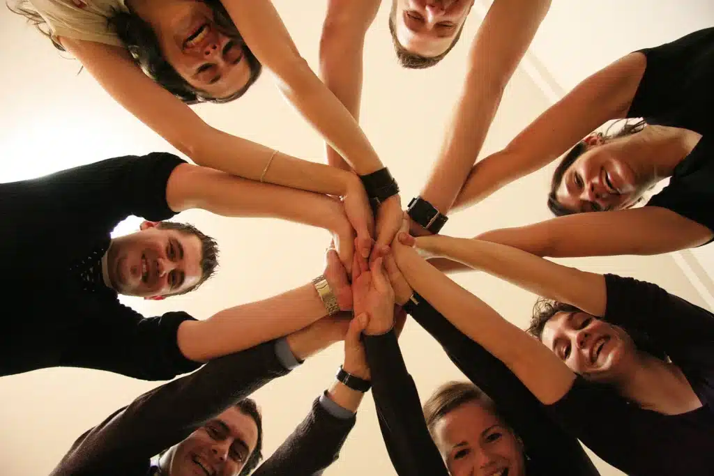 Gruppe junger Menschen bildet gemeinsam einen Kreis mit verschränkten Händen – Symbolbild für Zusammenhalt und positive Gruppenerfahrung in der Therapie für junge Erwachsene.