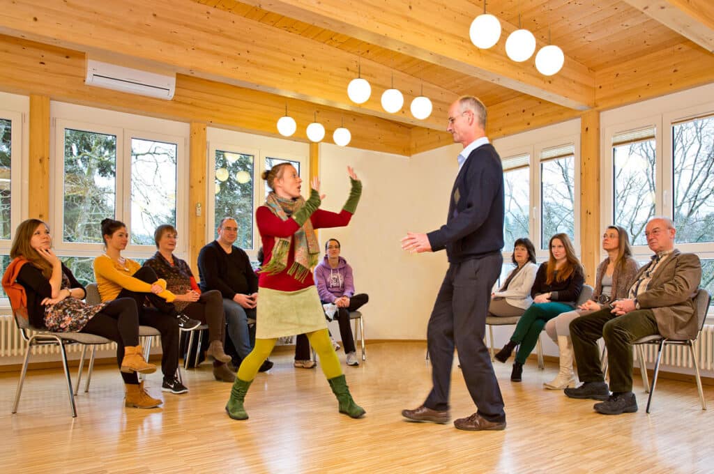 Gruppentherapiesitzung in einer Privatklinik für Depression. Zwei Personen stehen sich konfrontativ gegenüber, was symbolisch für das therapeutische Thema der Abgrenzung und Selbstbehauptung steht. Die Szene unterstreicht die Bedeutung von Raum, Körpersprache und Interaktion im geschützten Rahmen der Psychotherapie.