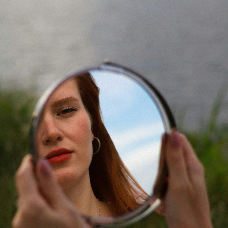 Selbstkritischer Blick einer jungen Frau in den Spiegel: symbolisiert den inneren Kampf mit dem Selbstbild bei Bulimie - vor einer Therapie in Bulimie Klinik am Leisberg.