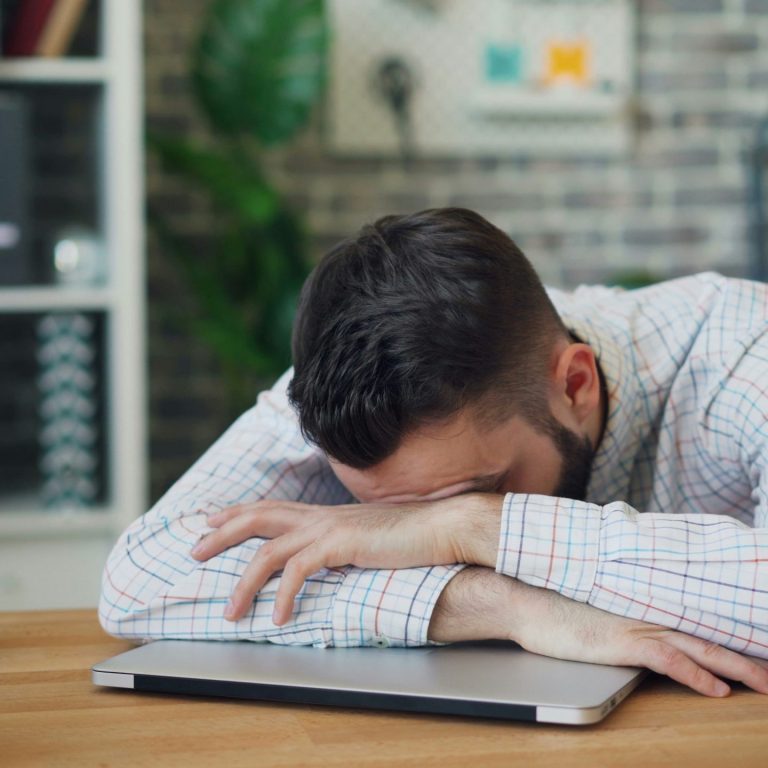 Erschöpfter Mann am Arbeitsplatz legt den Kopf auf den Tisch – Symbolbild für Schlafprobleme, behandelt in der Schlafstörungen Privatklinik Baden-Baden